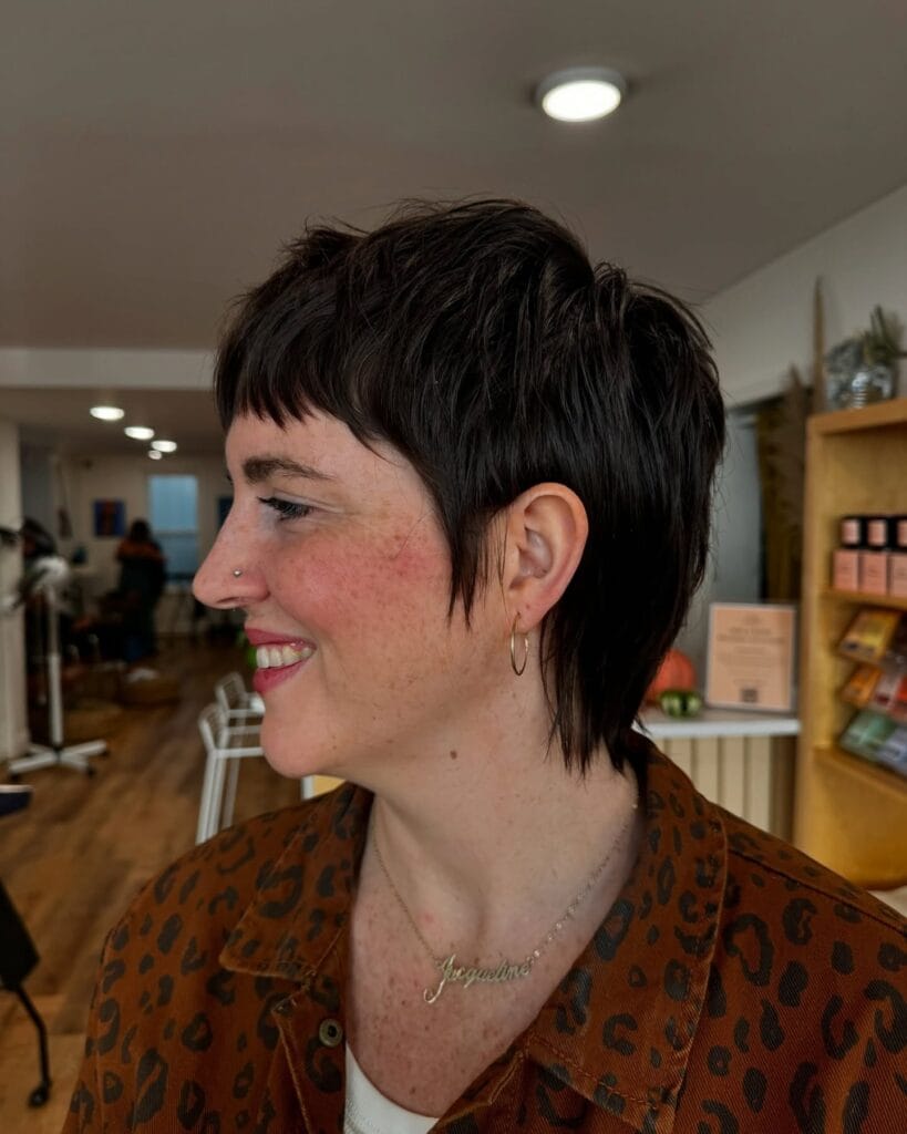 A short tomboy haircut with a clean undercut and longer top brushed back in a sleek style.