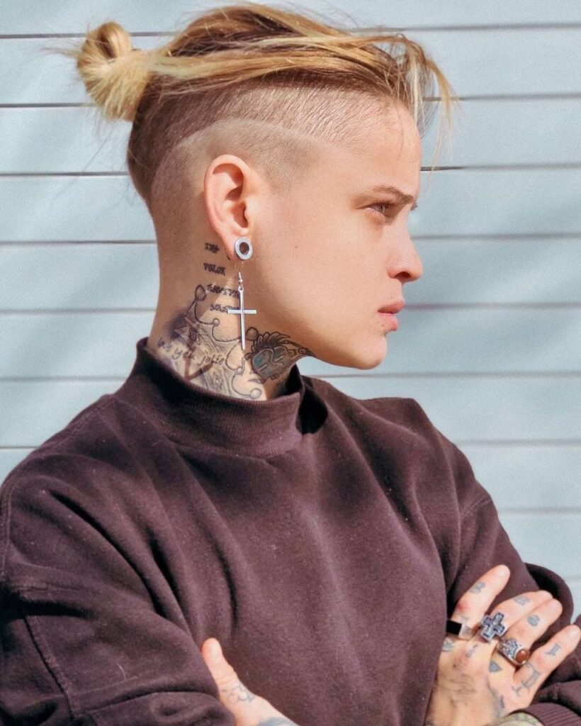 A woman with a tomboy undercut hairstyle featuring shaved sides and a textured top tied into a small knot.