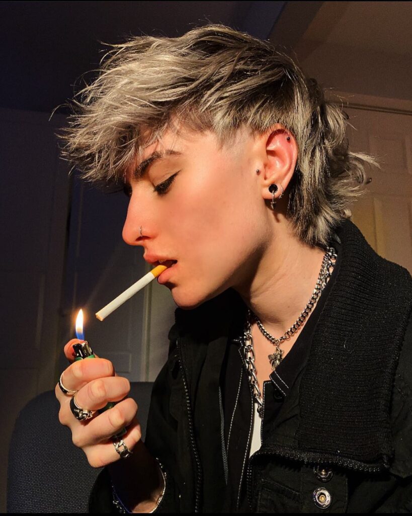 A woman with a textured tomboy mullet haircut featuring choppy layers, short sides, and a longer back.