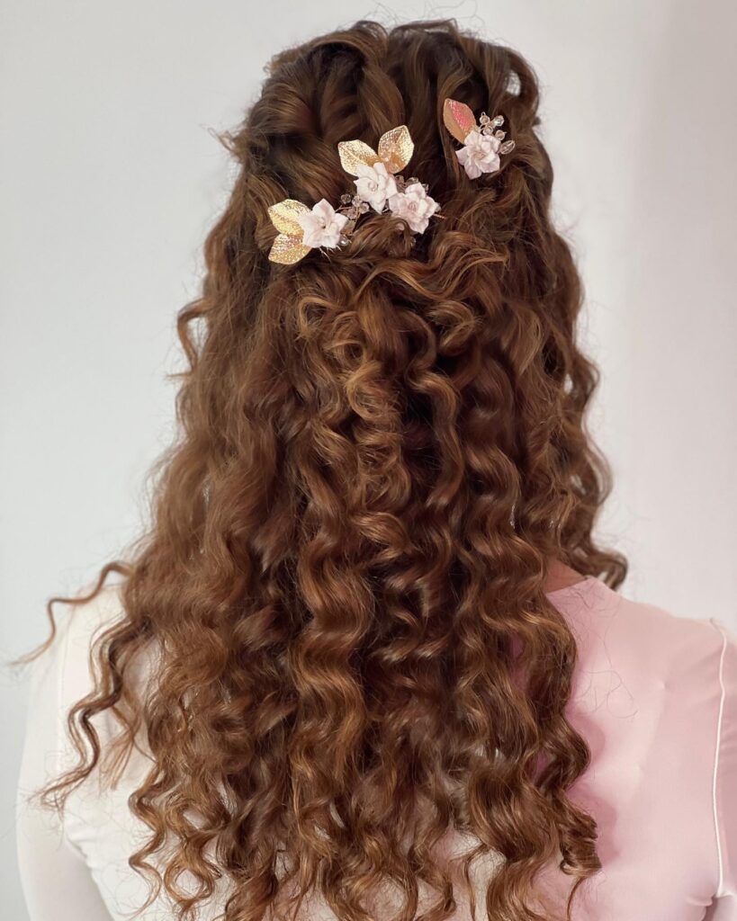 Long curly brown hair styled in a half up twist with floral hair accessories and defined curls.