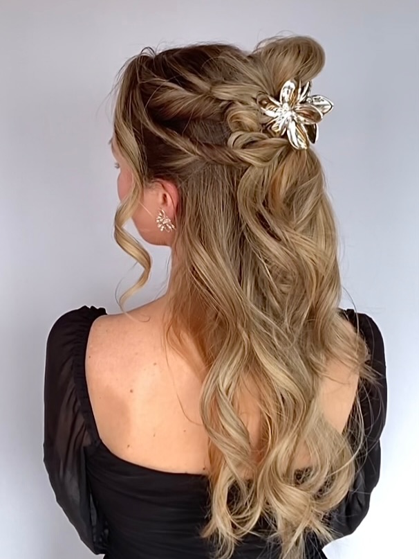 Long blonde wavy hair styled with a braid and secured with a gold clip in a half up style.