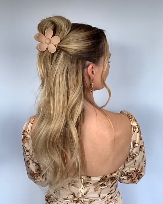 Long blonde wavy hair styled half up with a large flower clip at the back.