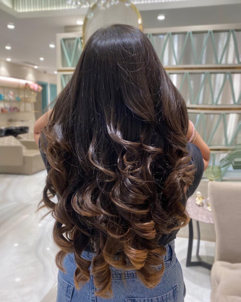 Long dark brown layered hair with soft curled ends and a smooth glossy finish.