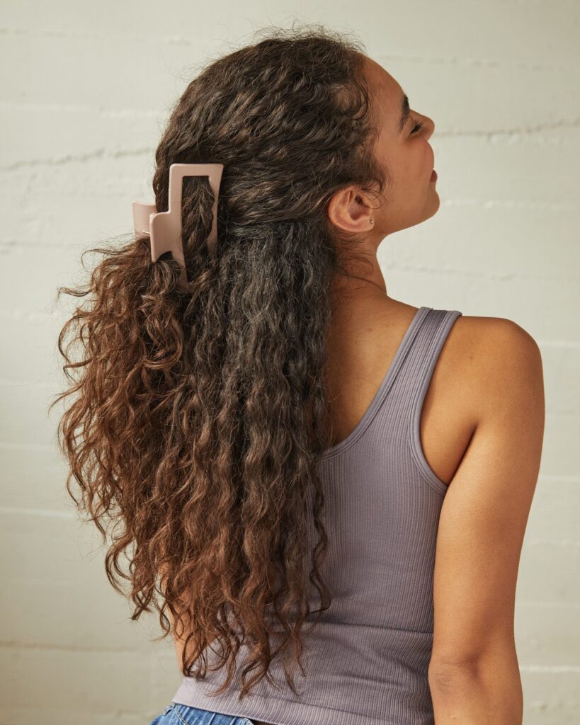 Long curly hair styled in a half ponytail with a large claw clip and natural texture.