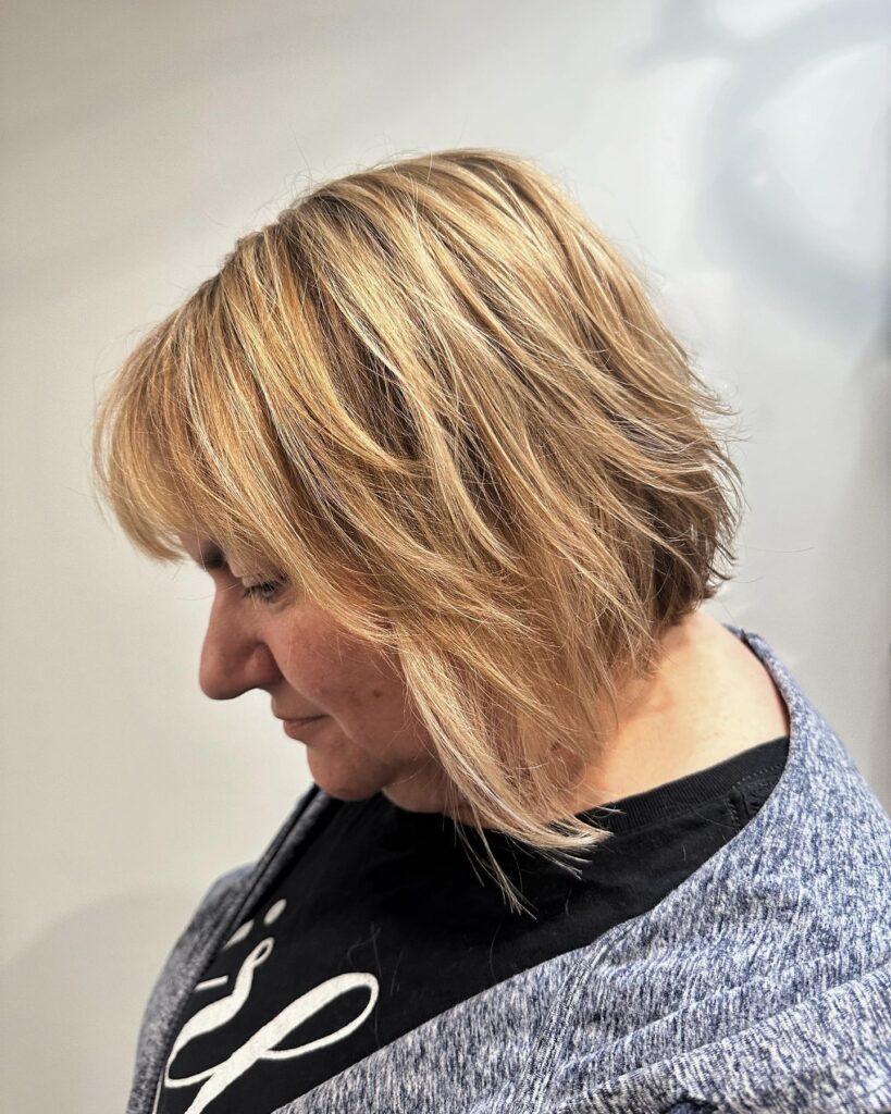 A warm blonde textured bob with side swept bangs and layered ends.