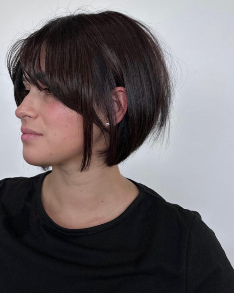 A sleek brunette textured bob with long side bangs and a softly layered shape.