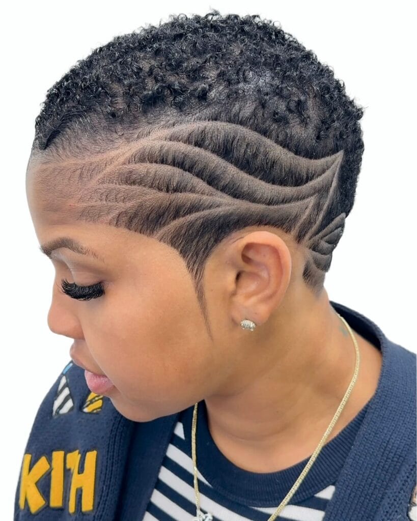 A short buzzed tomboy haircut with natural curls on top and shaved wave design on the sides.