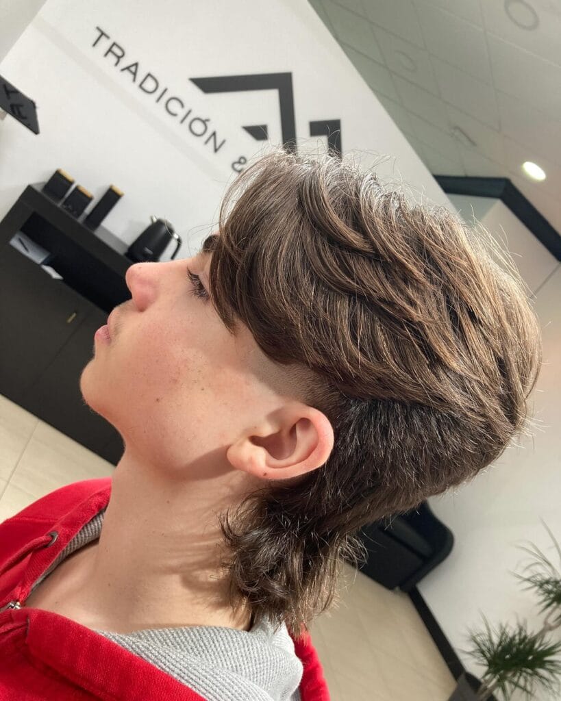 A layered tomboy mullet with a short top, undercut sides, and longer textured back in medium brown hair.