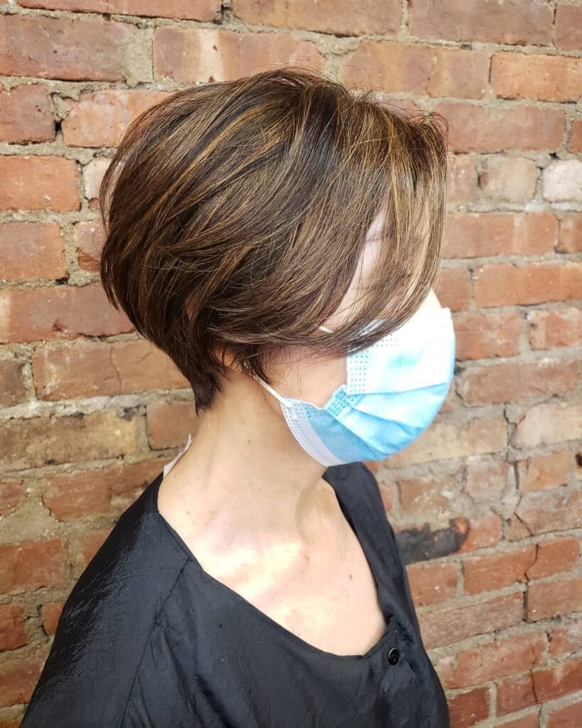 A short layered tomboy bob with a tapered nape and soft light brown highlights styled with natural texture.