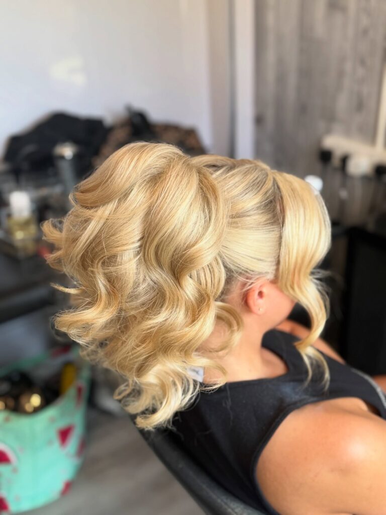 Long platinum blonde hair styled in a high voluminous ponytail with large soft waves and a smooth front.