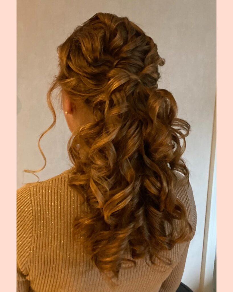 Long brown hair styled in a half up voluminous curly ponytail with soft defined curls.