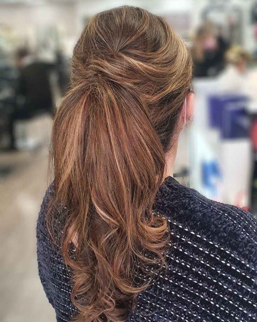 Long brunette hair styled in a sleek ponytail with softly curled ends and a smooth crown.