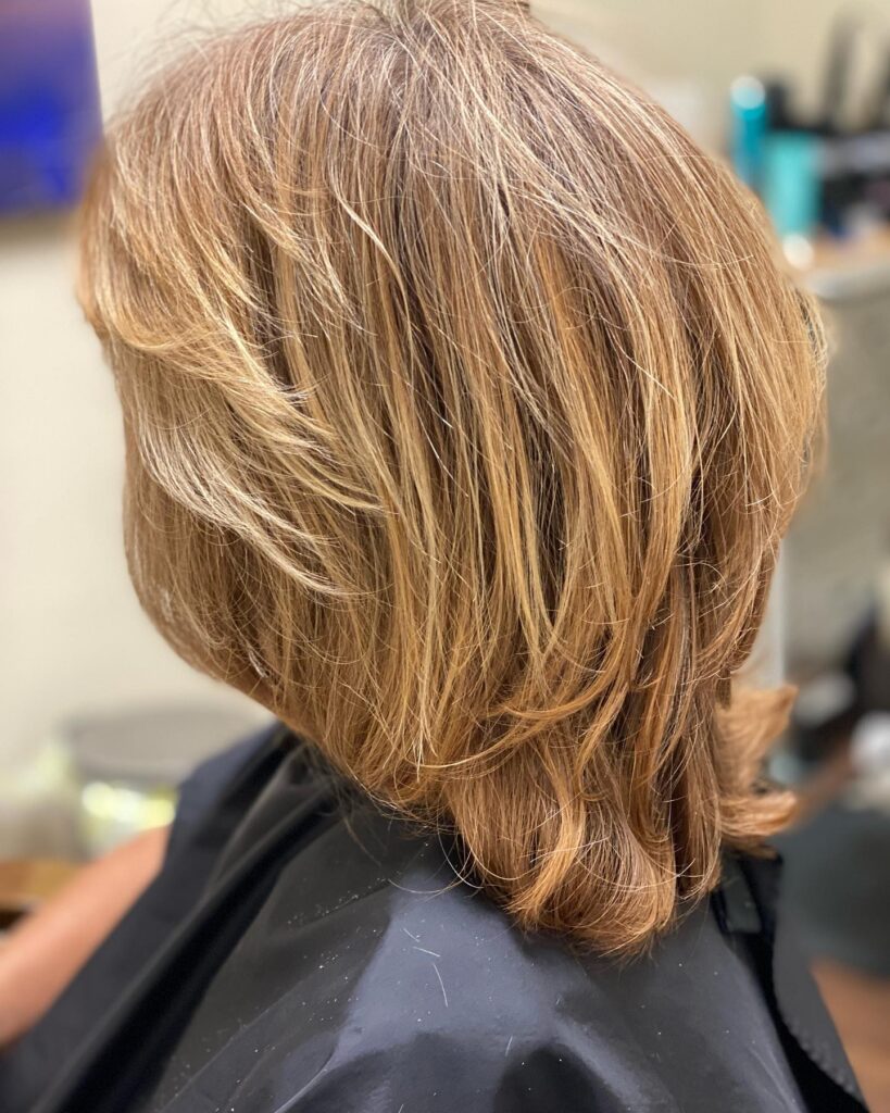 A shoulder length layered haircut with feathered ends, side bangs, and warm honey highlights.