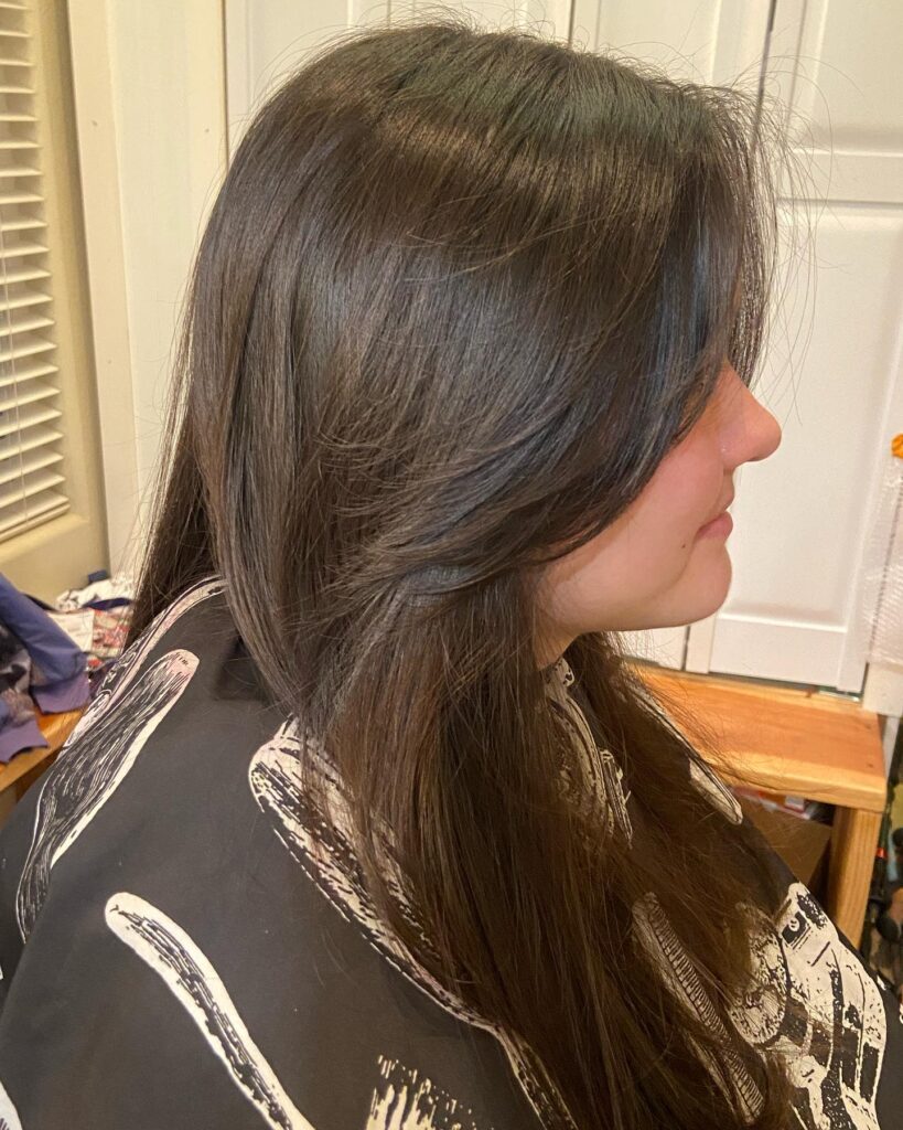 Long dark brown layered hair with side swept feathered bangs and soft volume.