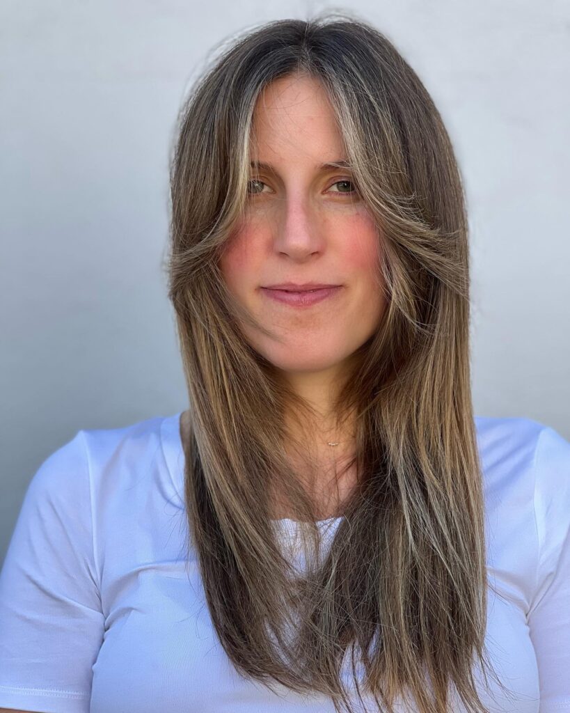 Long layered brown hair with soft feathered curtain bangs and natural volume.