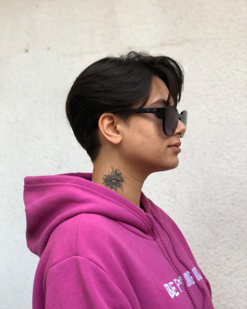 Short dark tomboy haircut with tapered sides and a smooth side swept top worn with sunglasses.