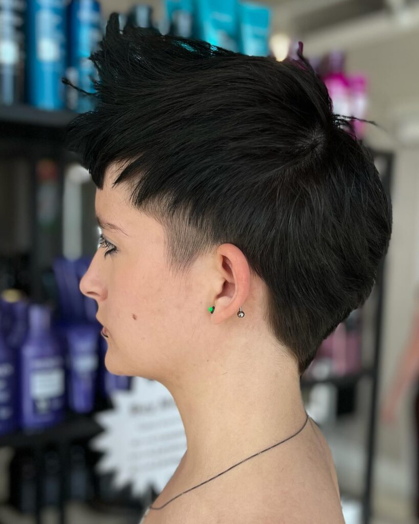 Short dark tomboy pixie haircut with shaved sides and a spiky textured top.