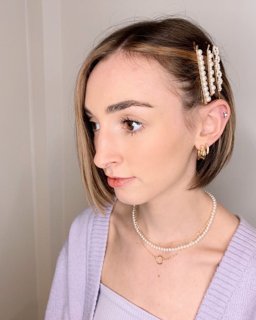 A woman with a straight chin-length brunette bob wears three stacked pearl bobby pins along a deep side part.