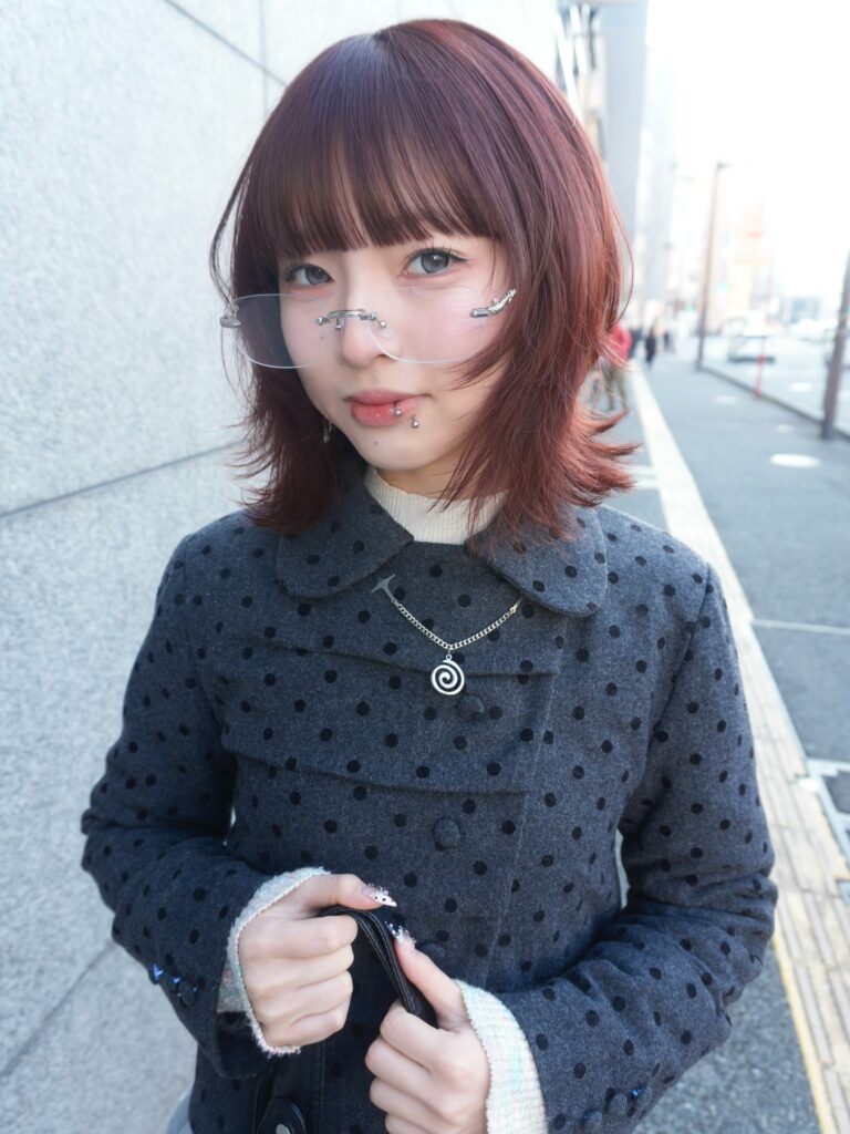 A woman with a chin length auburn bob featuring blunt bangs and flipped out ends.
