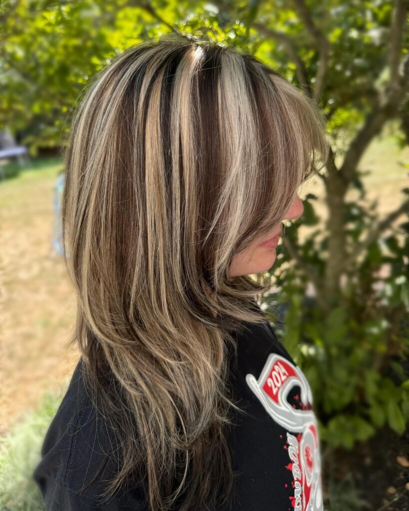 A woman with long layered dark brown hair featuring chunky bold blonde highlights.