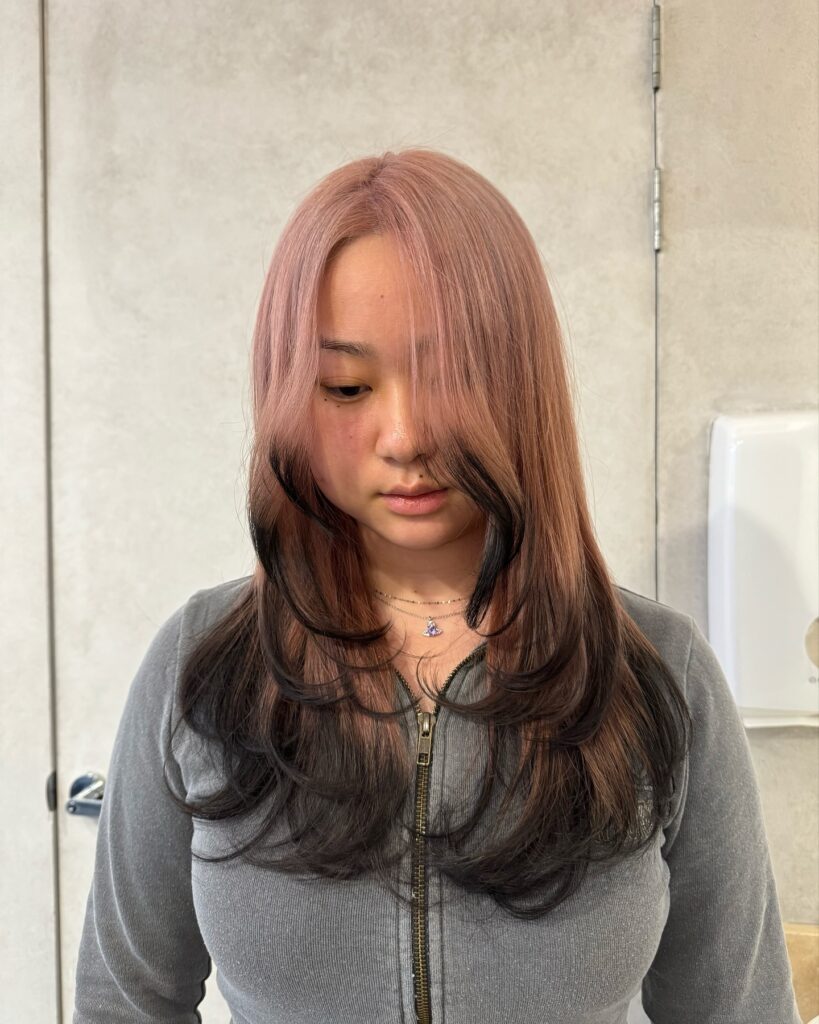 A woman with rose gold curtain bangs and face framing flipped out layers.