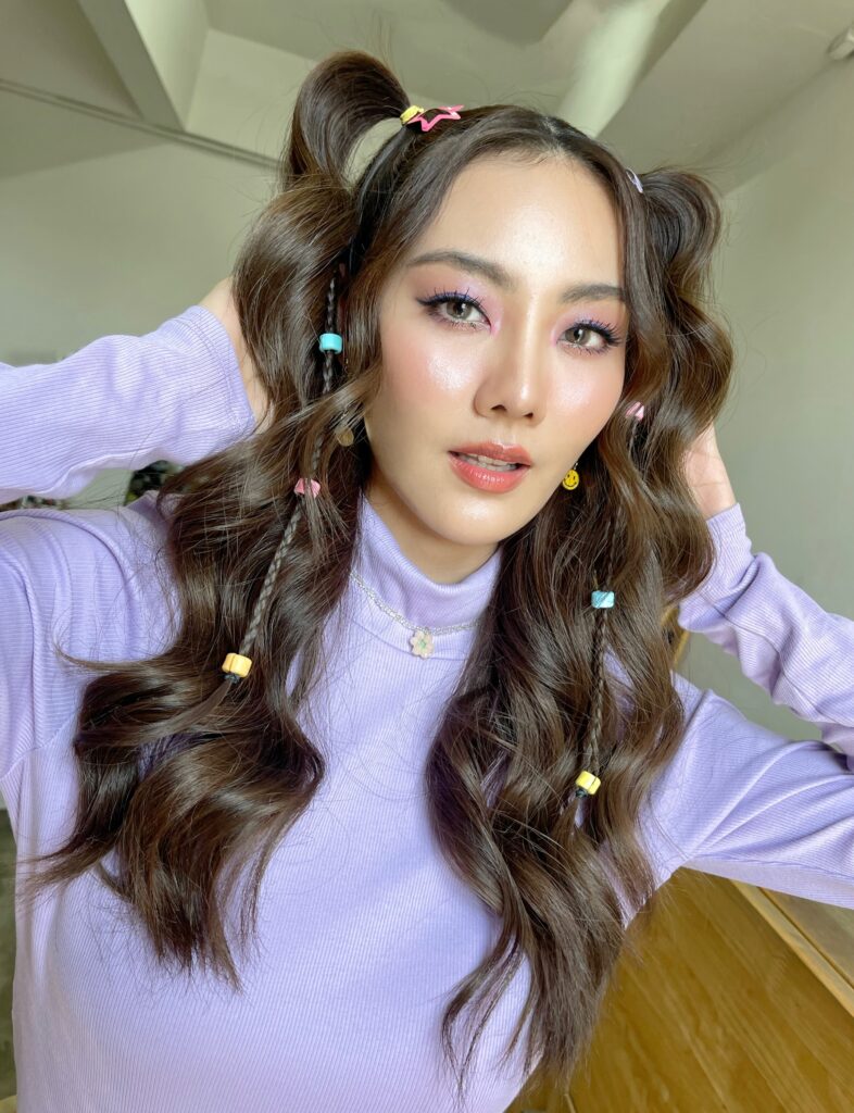 A woman with half up bubble pigtails featuring beaded braids and colorful star clips.