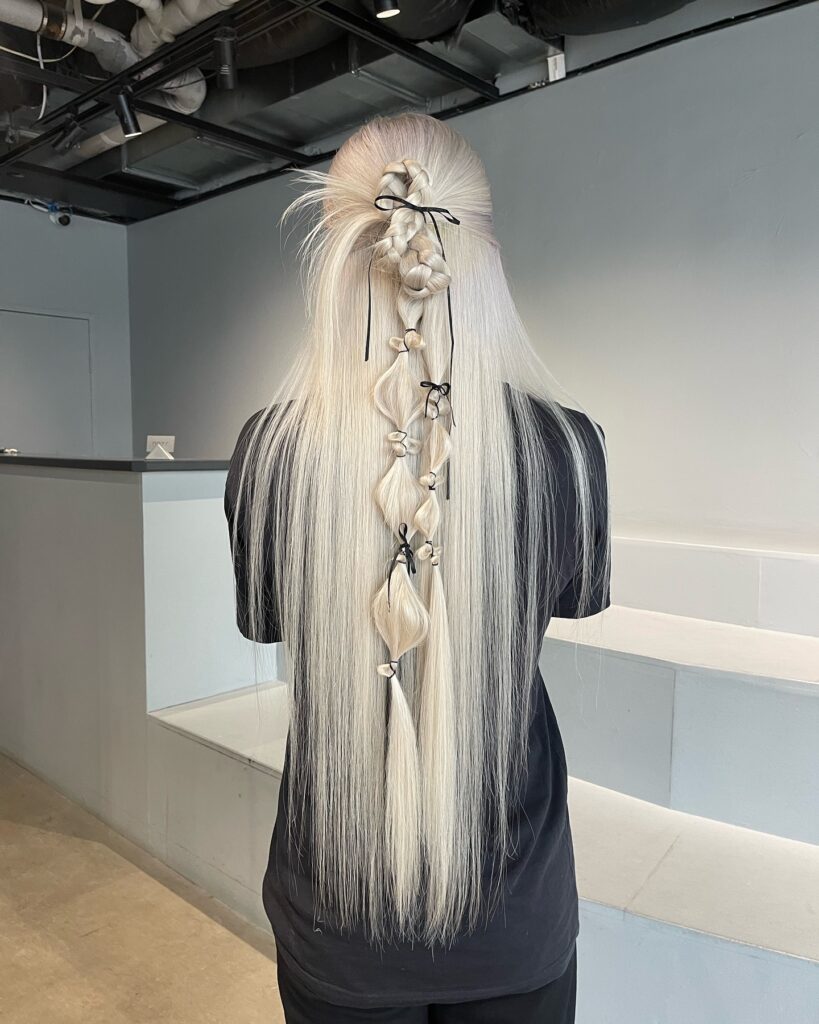 A woman with a platinum blonde bubble braid featuring black ribbon ties between each section.