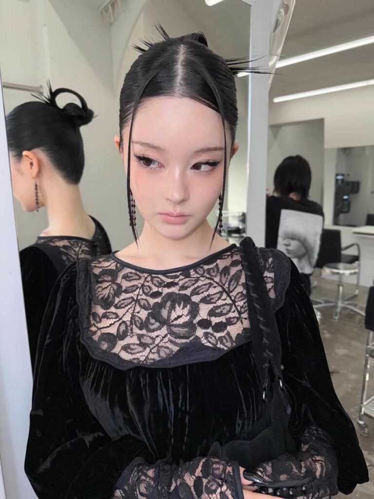 A woman with a sleek black high bun featuring two straight face-framing strands and spiky loose pieces at the crown.