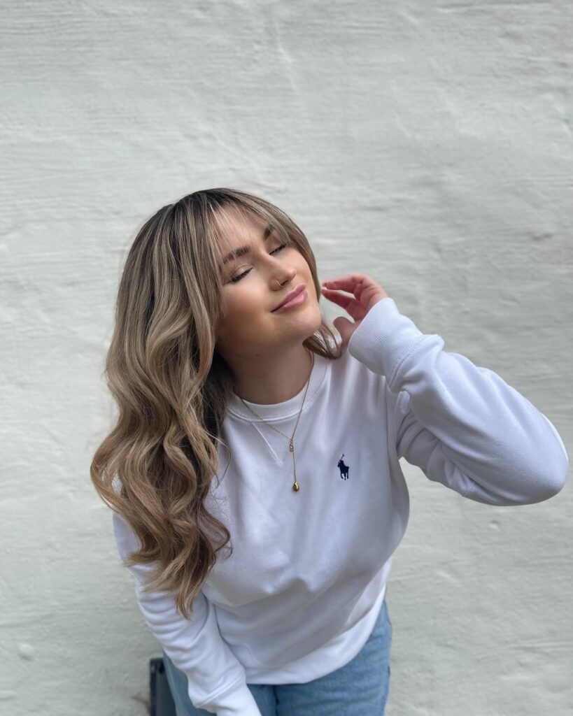 Long wavy hair with curtain bangs and a dark-root-to-caramel-blonde balayage color melt.