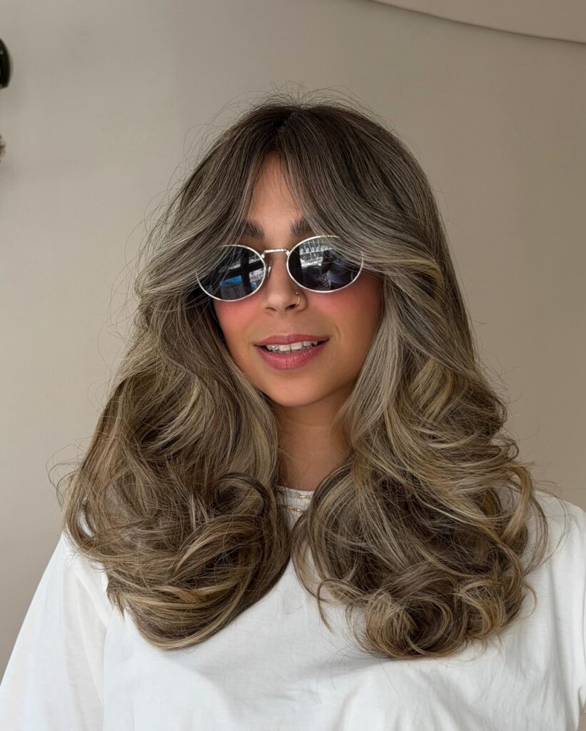 Layered hair with wispy bangs, bronde balayage color, and bouncy curls.