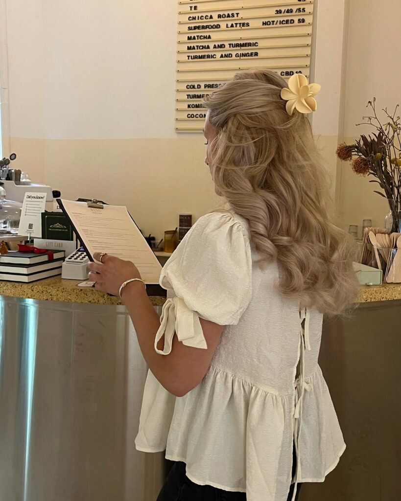 Long ashy blonde half up hairstyle with romantic curls and a flower hair clip.