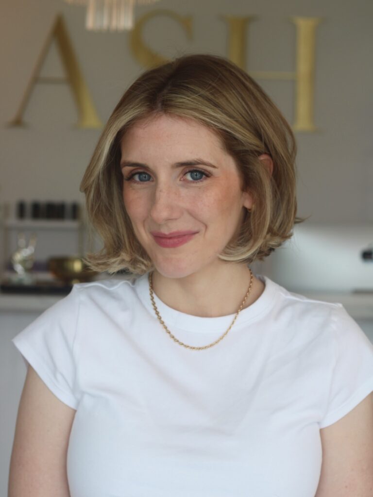 A woman with a blonde and honey toned chin length bob smiles in a portrait photo.