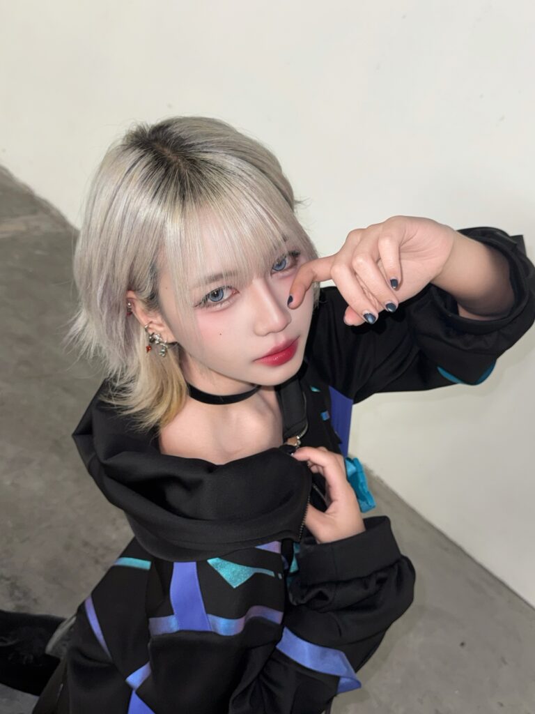 A woman with an icy platinum blonde bob and full bangs poses with dark roots showing at the part.