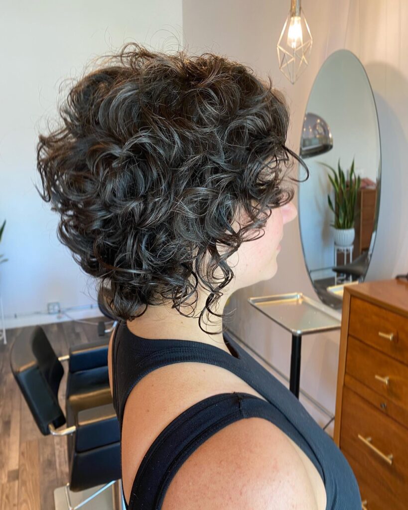 A woman with a short layered curly crop featuring natural salt and pepper brunette and gray tones.
