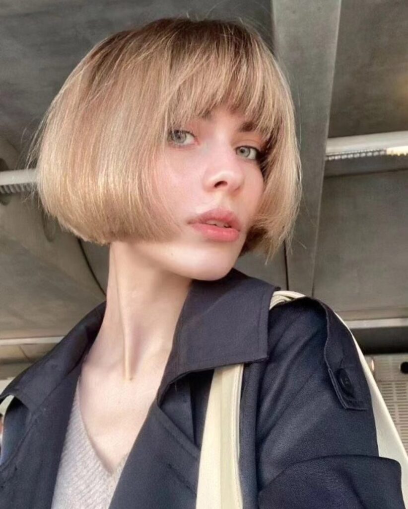 A woman with a sleek chin-length blonde blunt bob styled with a full straight-across fringe.