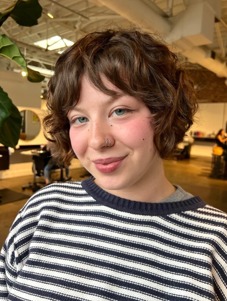 A woman with a chin-length curly brown bob styled with soft curtain bangs and choppy layers.