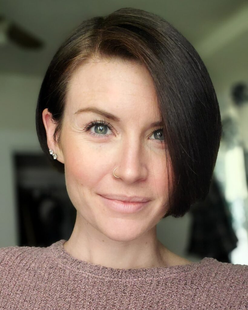 A woman with a sleek dark brunette bob and a deep side part smiles softly at the camera.
