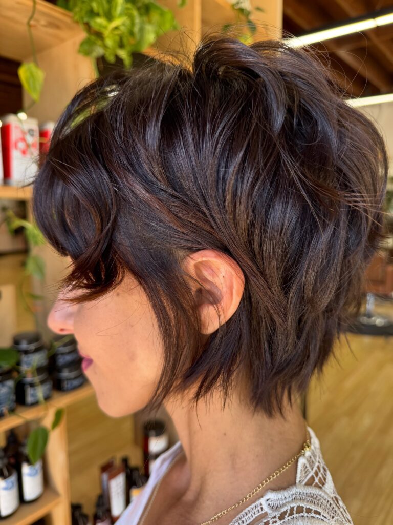 A woman with a tousled brunette wolf cut and face framing curtain layers shows off the side view of her hair.
