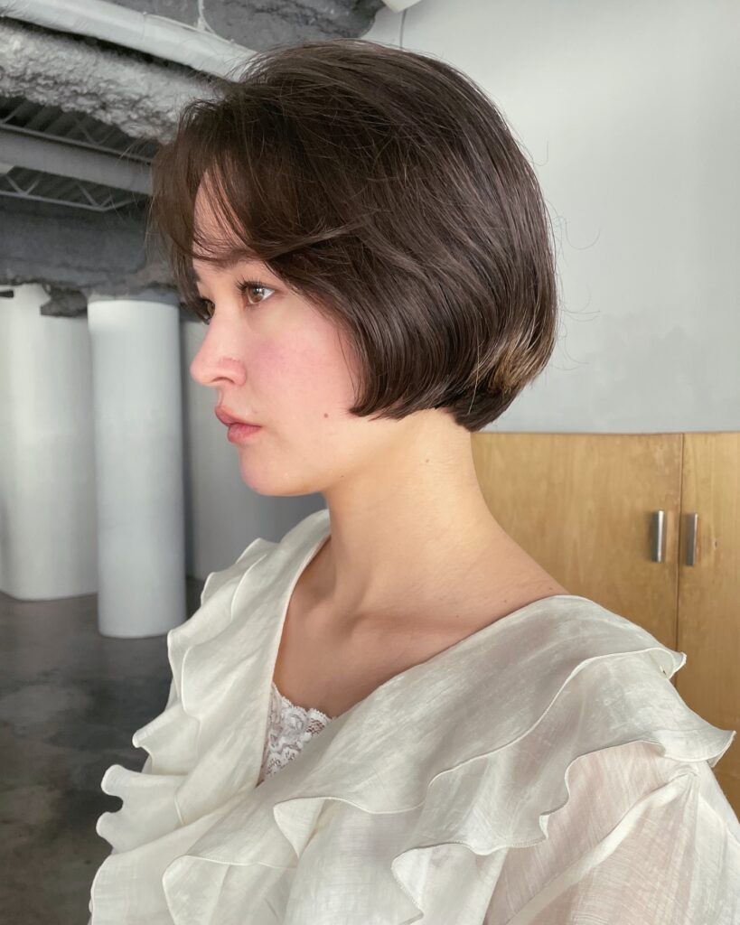 A woman with a rounded chestnut brown bob and wispy fringe wears a ruffled cream blouse.