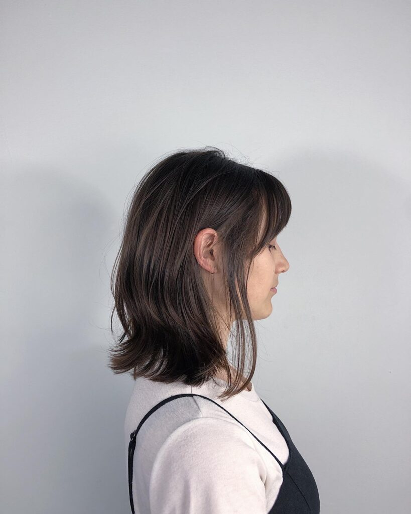 A woman with a shoulder length brunette lob featuring curtain bangs and soft, piecey layered ends.