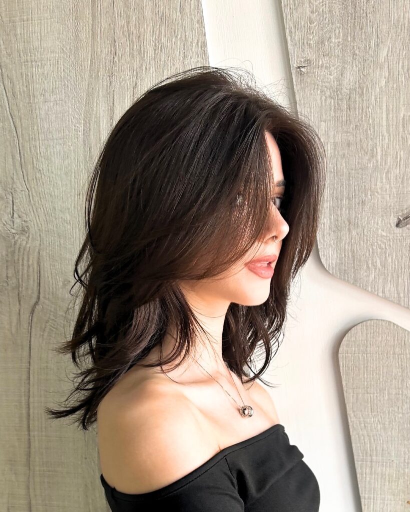 A woman with deep brown, voluminous wavy hair featuring long side swept curtain layers.