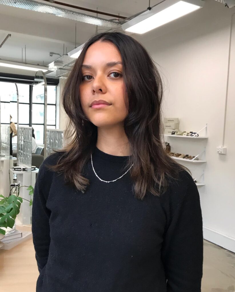 A woman with medium length brunette hair styled into a textured, undone shag with face framing layers.