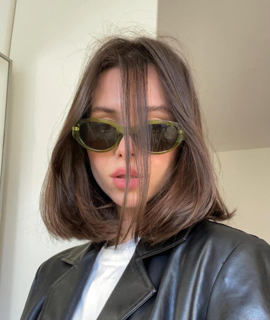 A woman wearing sunglasses with a sleek, chin length brown bob parted in the middle.