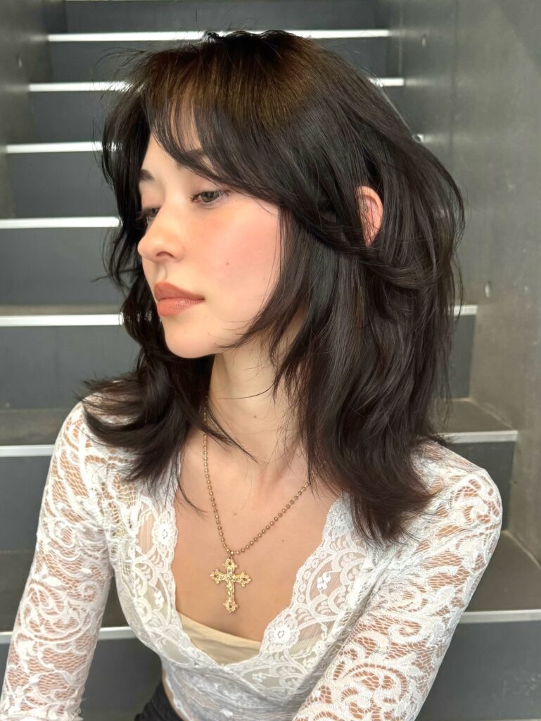 A woman with a dark brunette shag haircut featuring feathered layers and wispy bangs.
