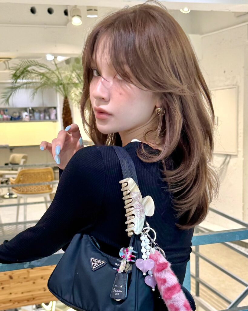 A woman with medium length ash brown hair featuring airy curtain bangs and soft, feathery layered ends.