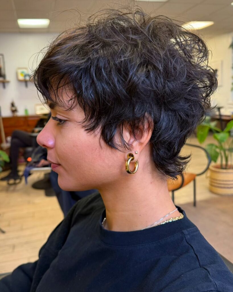 A woman with a voluminous curly espresso brown pixie shag shows off gold hoop earrings in profile.