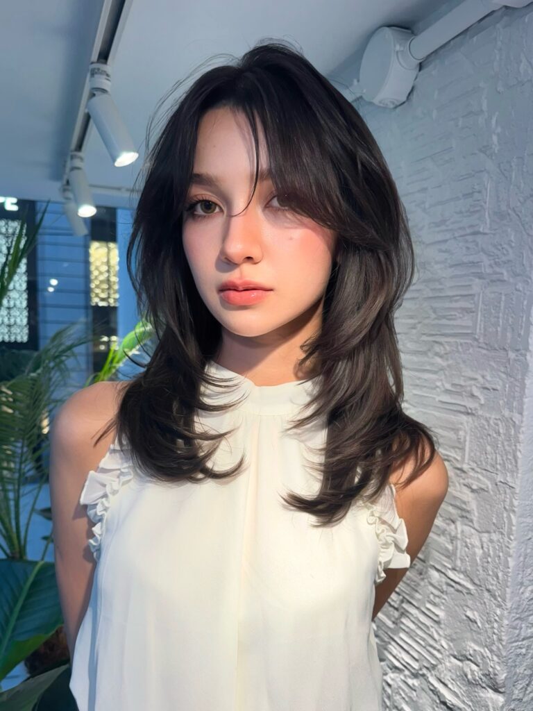 A woman with a dark brunette medium short layered hairstyle and curtain bangs with a soft blowout finish.