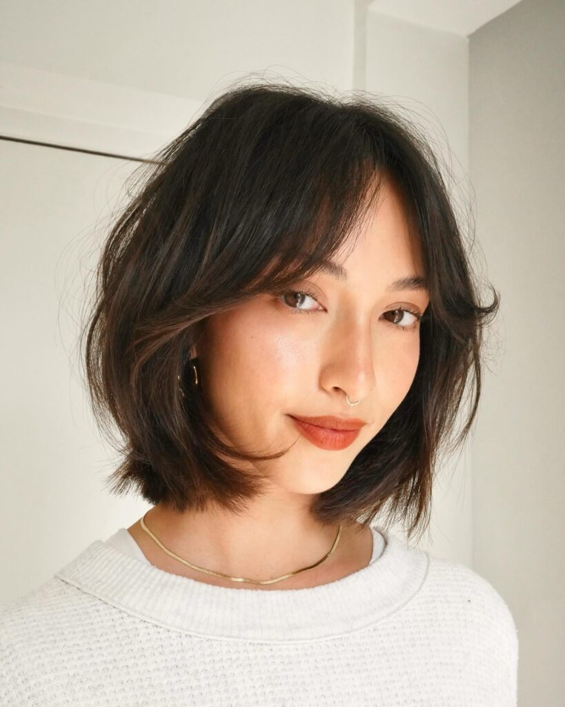 A woman with dark brown chin length bob and soft curtain bangs smiling at the camera.