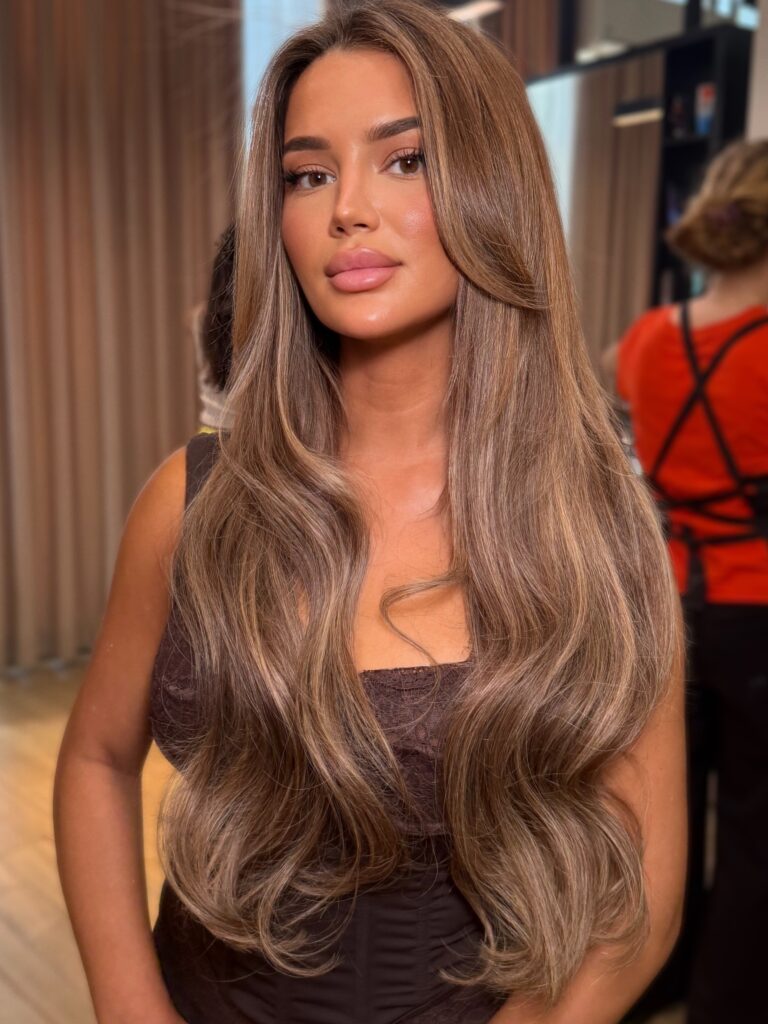 Extra long light brown hair with balayage highlights styled in soft beachy waves.