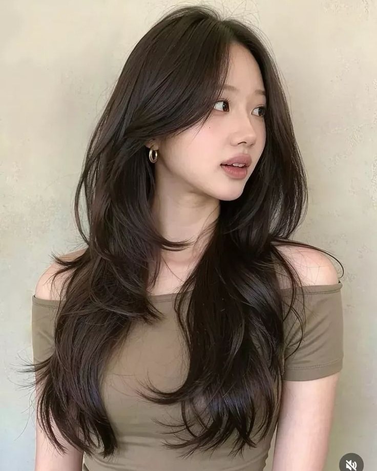 Long dark brown hair styled with face-framing curtain bangs and soft flicked-out layers.